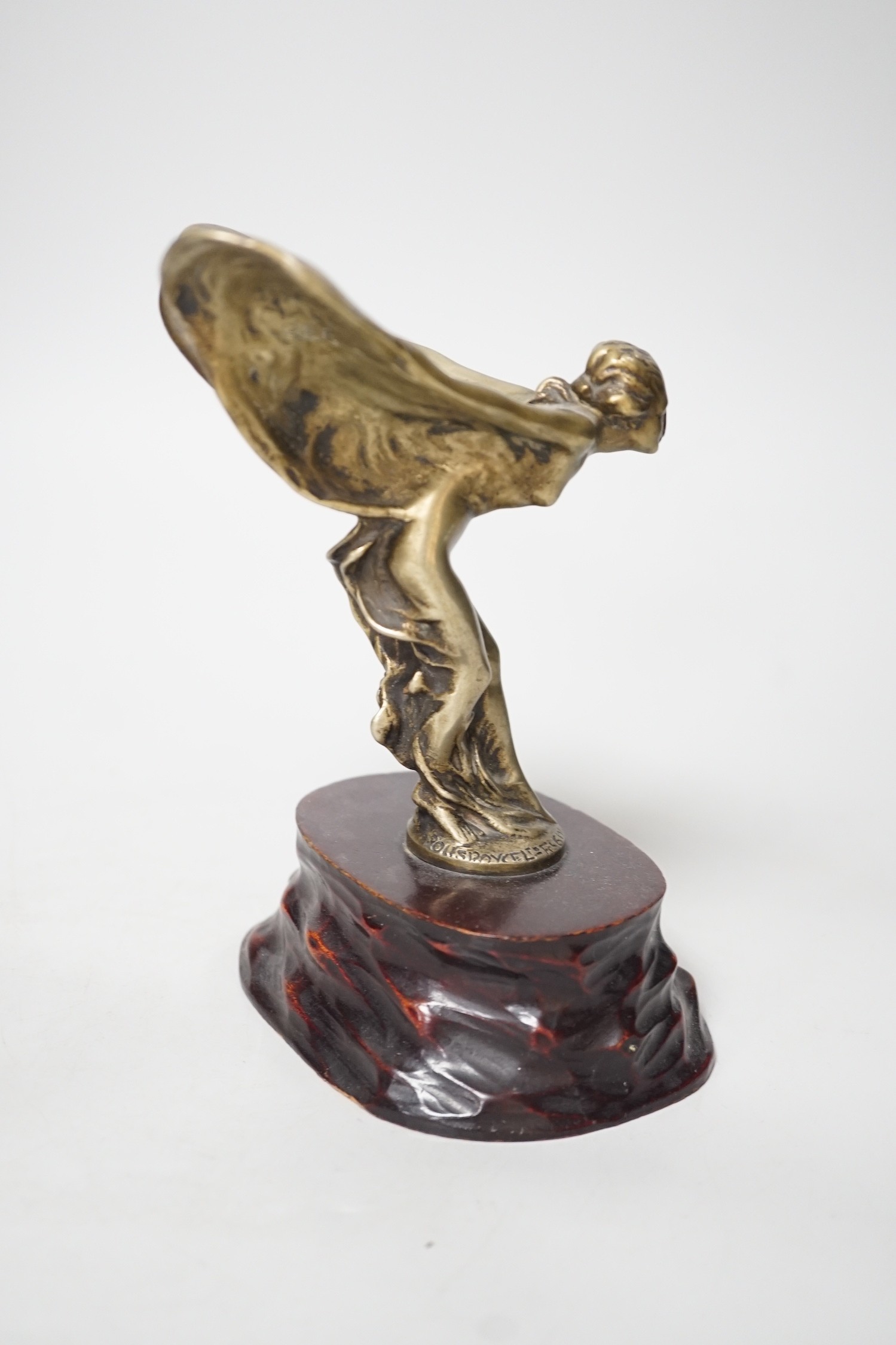 After Charles Sykes, a gilt metal Rolls Royce car mascot - ‘’Spirit of Ecstasy’’, inscribed and bearing date 1911, on a carved wooden plinth. 17.5cm tall